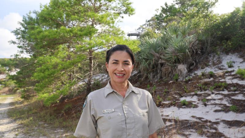 A smiling park ranger in front of sand dunes.